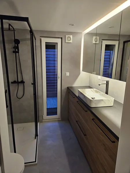 Elegantes Badezimmer in einem schlüsselfertigen Bungalow der MONO-Serie von Compact Haus mit bodengleicher Glasdusche, großem Holzwaschtisch und LED-beleuchtetem Spiegel.