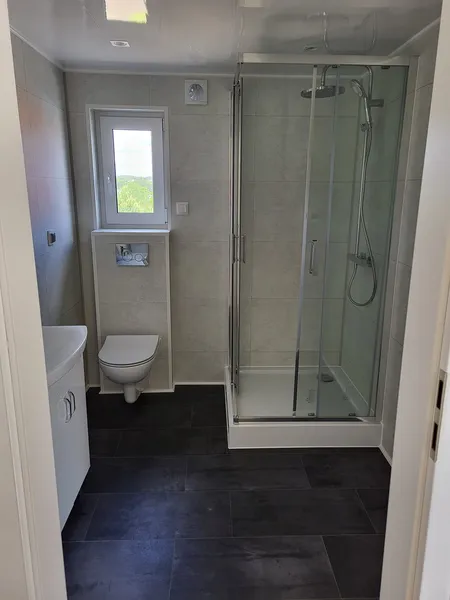Modern gestaltetes Badezimmer der MONO-Serie von Compact Haus mit Eck-Glasdusche, dunklem Fliesenboden und pflegeleichter Ausstattung.