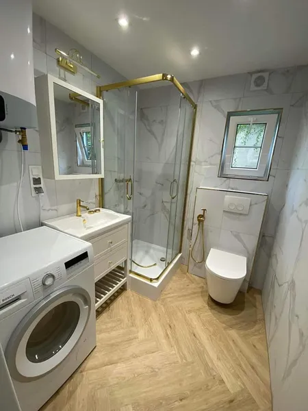 Luxuriöses Badezimmer in einem winterfesten Bungalow der MONO-Serie von Compact Haus mit goldenen Armaturen, Marmoroptik-Fliesen und Waschmaschine.