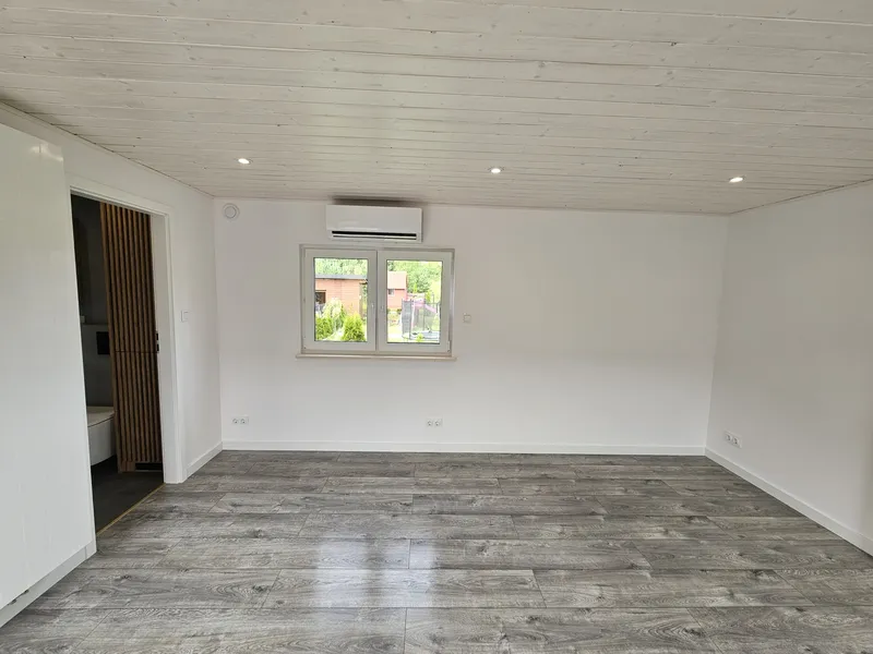 Geräumiger Wohnbereich im modernen skandinavischen Stil in einem winterfesten Bungalow der MONO-Serie von Compact Haus mit Klimaanlage, Holzoptikboden und weiß lasierter Decke.