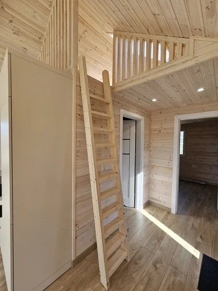 Heller Innenbereich im Loft-Stil in einem winterfesten Bungalow der MONO-Serie von Compact Haus mit Schlafgalerie, Holzleiter und Naturholzverkleidung.