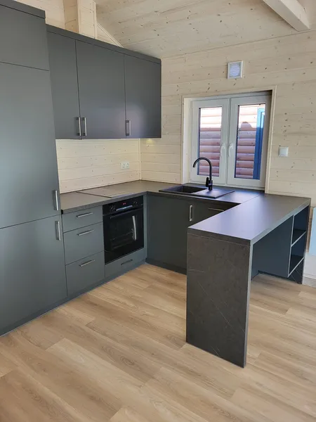 Moderne anthrazitfarbene Einbauküche in U-Form mit integrierter Küchentheke, schwarzer Spüle und Backofen in einem hellen Bungalow der MONO-Serie.