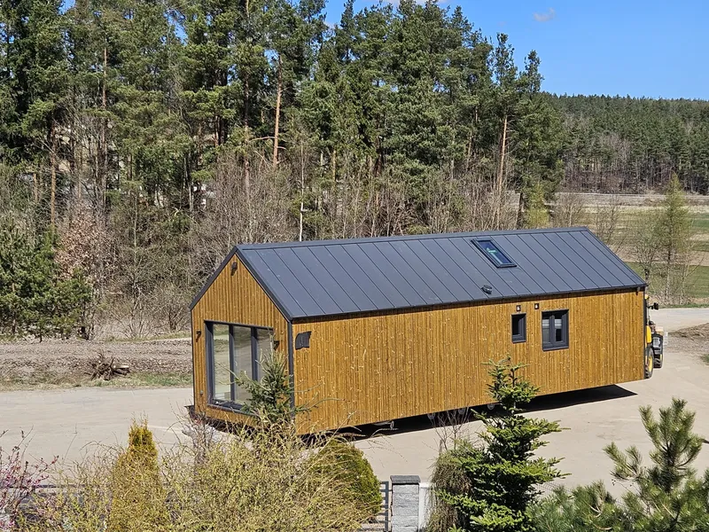 Schlüsselfertige Anlieferung eines winterfesten Ferienhauses der MONO-Serie von Compact Haus mit Holzfassade, Satteldach, Dachfenster und großer Glasfront.
