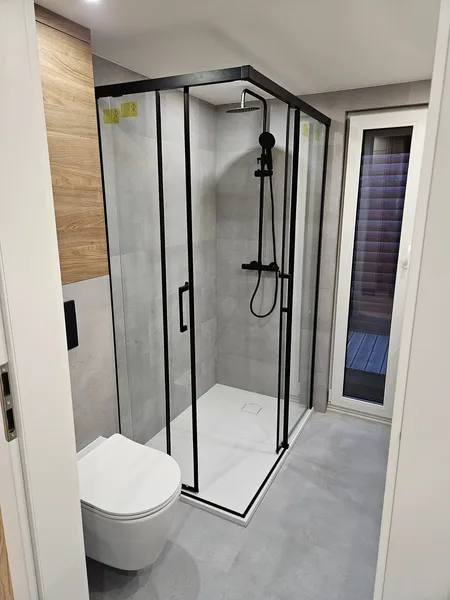 Modernes Badezimmer in einem winterfesten Ferienhaus der MONO-Serie von Compact Haus mit großer Eck-Glasdusche, Regendusche und hellgrauen Fliesen.