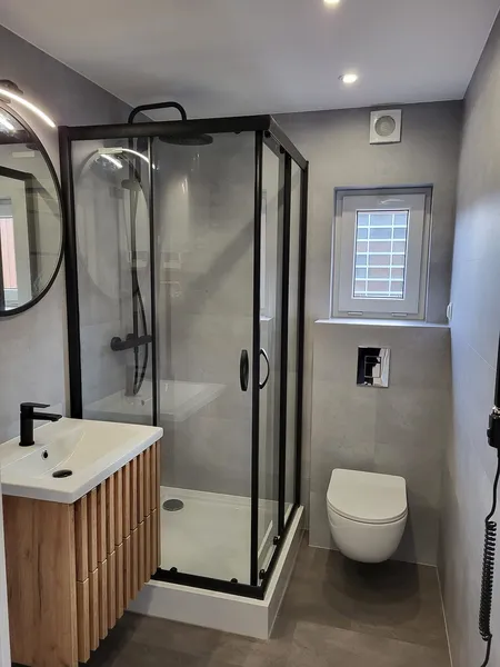 Modernes Badezimmer in einem winterfesten Ferienhaus der MONO-Serie von Compact Haus mit Holzwaschtisch, LED-Spiegel und Glasdusche mit schwarzen Profilen.