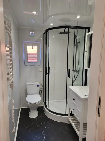 Gemütliches Badezimmer in einem winterfesten Ferienhaus der MONO-Serie von Compact Haus mit Eck-Glasdusche, dunklem Marmorboden und Waschtisch im Landhausstil.