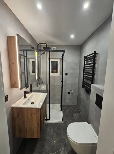 Exklusives Badezimmer in einem winterfesten Ferienhaus der MONO-Serie von Compact Haus mit Holzwaschtisch, barrierefreier Glasdusche und dunklen Fliesen in Marmoroptik.