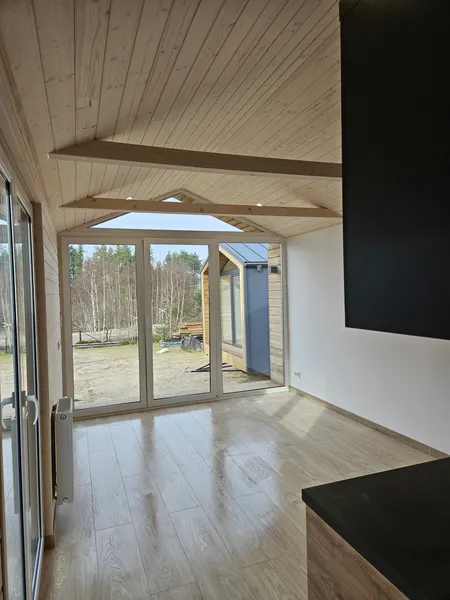 Heller Wohnbereich im skandinavischen Stil in einem winterfesten Ferienhaus der MONO-Serie von Compact Haus mit bodentiefer Fensterfront, Schiebetür und sichtbaren Holzbalken.