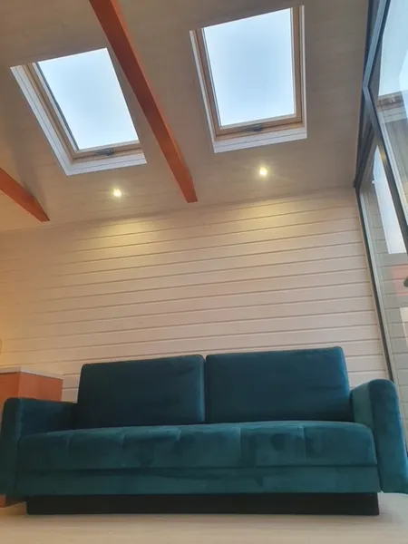 Gemütliche Kaminecke im skandinavischen Stil in einem winterfesten Ferienhaus der MONO-Serie von Compact Haus mit Samtsofa, Dachfenstern und Echtholzverkleidung.