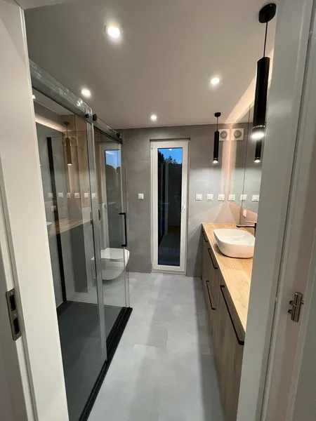 Modernes Luxus-Badezimmer in einem winterfesten Minihaus der MONO-Serie von Compact Haus mit großzügiger Glasdusche, Holzwaschtisch und bodentiefer Glastür.
