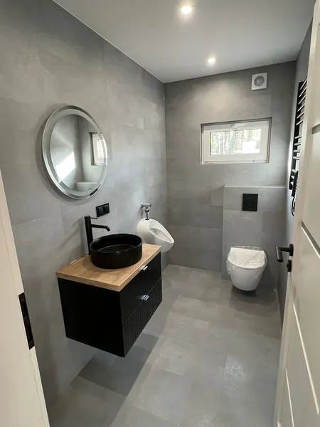 Modern gestaltetes Badezimmer in einem schlüsselfertigen Minihaus der MONO-Serie von Compact Haus mit schwarzem Aufsatzwaschbecken, LED-Spiegel und mattgrauen Fliesen.