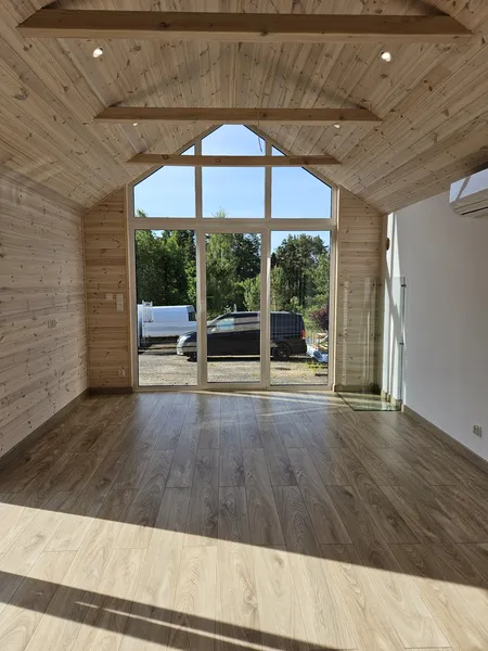 Lichtdurchfluteter Wohnbereich im skandinavischen Stil in einem Minihaus der MONO-Serie von Compact Haus mit giebelhoher Fensterfront, Echtholzverkleidung und Klimaanlage.