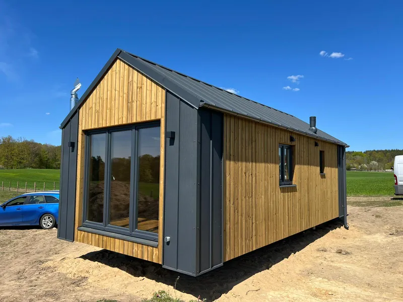 Modernes winterfestes Minihaus der MONO-Serie von Compact Haus mit vertikaler Holzfassade, anthrazitfarbener Blechverkleidung und großer bodentiefer Glasfront.