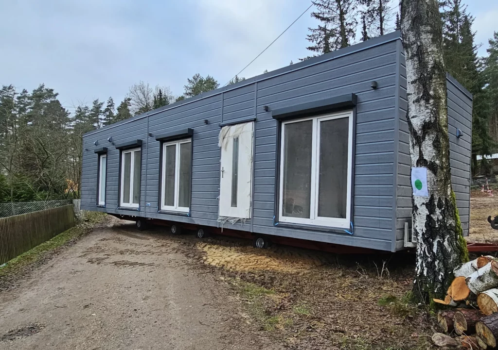 Modernes winterfestes Mobilheim der MONO-Serie von Compact Haus mit anthrazitgrauer Kunststoff-Fassade in Holzoptik, bodentiefen Fenstern und Rollläden.