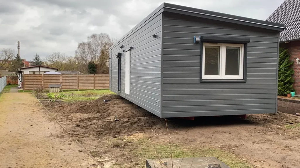 Anlieferung und Aufstellung eines modernen Mobilheims von Compact Haus mit grauer Fassade und Pultdach auf einem Kundengrundstück.