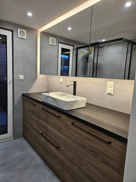 Edler Waschbereich in einem schlüsselfertigen Mobilheim der MONO-Serie von Compact Haus mit Holzunterschrank, Aufsatzwaschbecken in Marmoroptik und beleuchtetem Spiegelschrank.