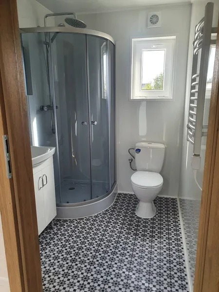 Kompaktes Badezimmer der MONO-Serie von Compact Haus mit Mosaikboden, Eck-Glasdusche, Handtuchheizkörper und pflegeleichter Ausstattung.