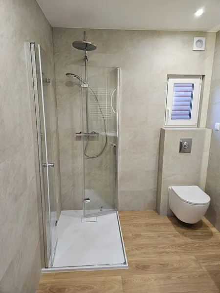 Helles, barrierefreies Badezimmer in einem winterfesten Mobilheim der MONO-Serie von Compact Haus mit Glasdusche, Holzoptikboden und beigen Wandfliesen.