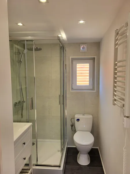 Helles Badezimmer in einem winterfesten Mobilheim der MONO-Serie von Compact Haus mit Eck-Glasdusche, Chromarmaturen und Handtuchheizkörper.