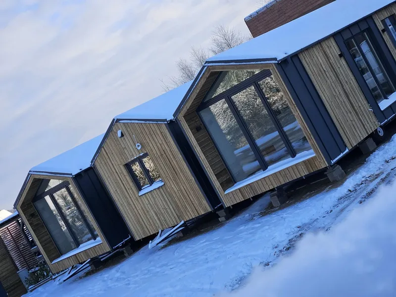 Winterfestes Mobilheim im Barnhouse-Stil von Compact Haus mit Satteldach, großen Panoramafenstern und Holzfassade.
