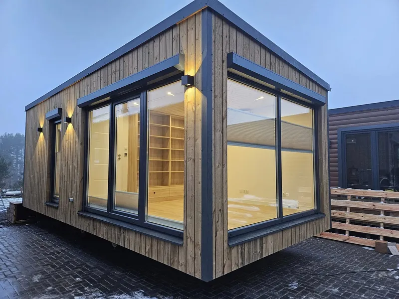 Luxuriöses Mobilheim von Compact Haus mit großer Eckverglasung, moderner Holzfassade und beleuchtetem Innenraum.