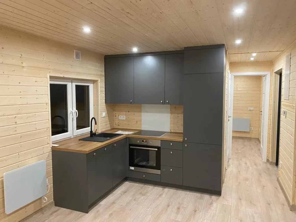 Moderne Einbauküche in U-Form im Mobilheim der MONO-Serie von Compact Haus mit anthrazitfarbenen Fronten, heller Arbeitsplatte in Holzoptik, integriertem Backofen, Kochfeld und LED-Unterbauleuchten.