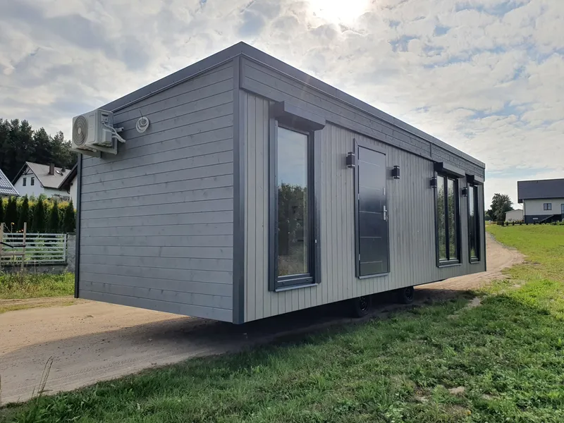 Modernes Mobilheim von Compact Haus mit Flachdach, grauer Holzfassade, Klimaanlage und bodentiefen Fenstern.