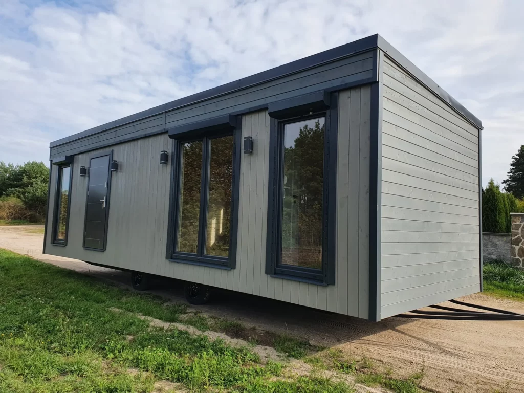 Modernes winterfestes Mobilheim der MONO-Serie von Compact Haus mit hellgrauer Außenfassade, anthrazitfarbenem Sockel und einer hölzernen Eingangstreppe.