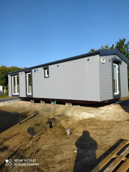 Modernes Mobilheim von Compact Haus in Hellgrau mit bodentiefen Fenstern während der Aufstellung auf dem Grundstück.