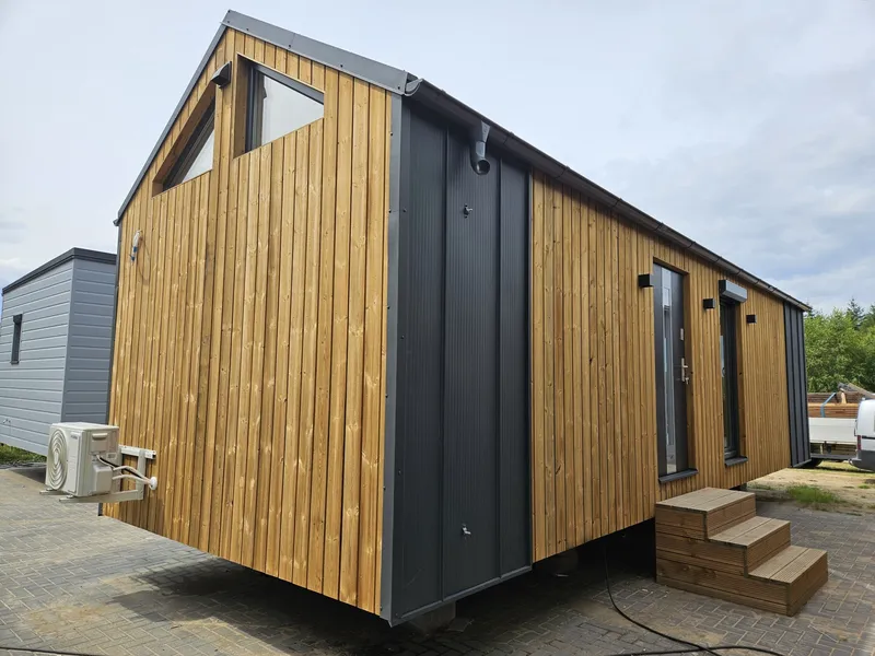 Winterfestes Mobilheim von Compact Haus in Holzständerbauweise mit vertikaler Holzfassade, Giebelfenstern und Klimaanlage.
