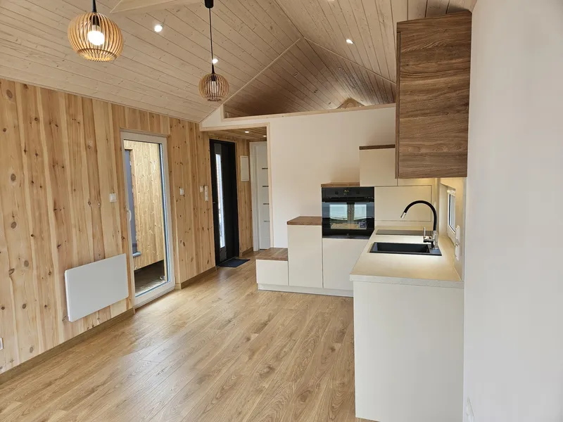 Moderner Wohn- und Küchenbereich im Loft-Stil in einem Mobilheim der MONO-Serie von Compact Haus mit Einbauküche, Treppenschrank und bodentiefer Fenstertür.
