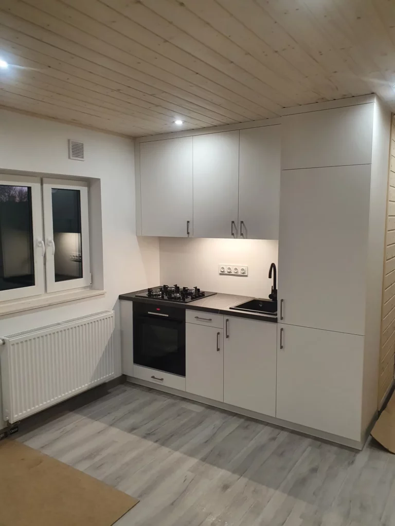 Moderne weiße Einbauküche mit Gasherd, Backofen und heller LED-Unterbauleuchte in einem Mobilheim der MONO-Serie von Compact Haus mit Holzdecke.