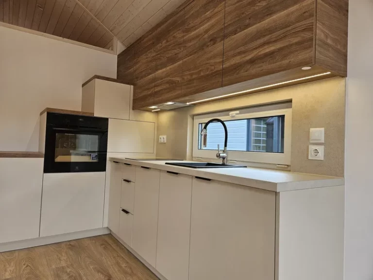 Moderne Einbauküche in einem Mobilheim der MONO-Serie von Compact Haus mit hellen Fronten, Oberschränken in Nussbaumoptik und integrierten Treppenstufen.