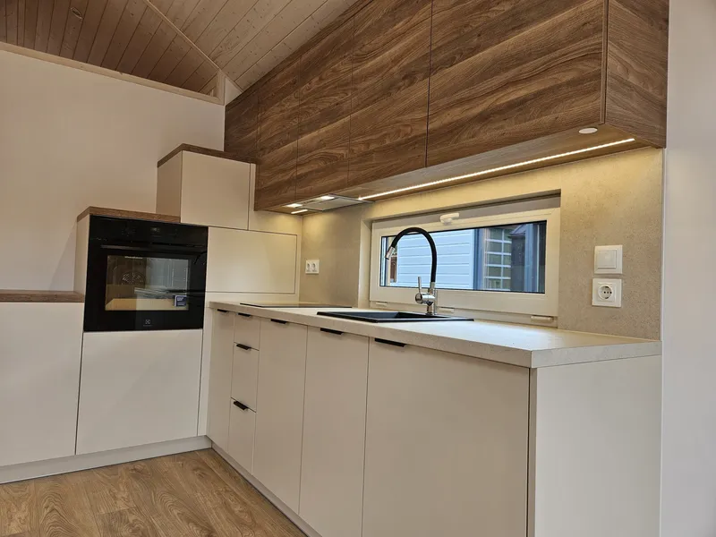 Moderne Einbauküche in einem Mobilheim der MONO-Serie von Compact Haus mit hellen Fronten, Oberschränken in Nussbaumoptik und integrierten Treppenstufen.