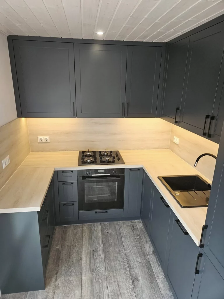 Moderne Einbauküche in U-Form im Mobilheim der MONO-Serie von Compact Haus mit anthrazitfarbenen Fronten, heller Arbeitsplatte in Holzoptik, integriertem Backofen, Kochfeld und LED-Unterbauleuchten.