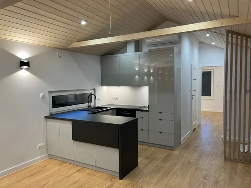 Moderne Einbauküche in U-Form mit grauen Hochglanzfronten, einer dunklen Arbeitsplatte, integrierter Klimaanlage und stilvoller Wandbeleuchtung in einem Compact Haus der MONO-Serie.