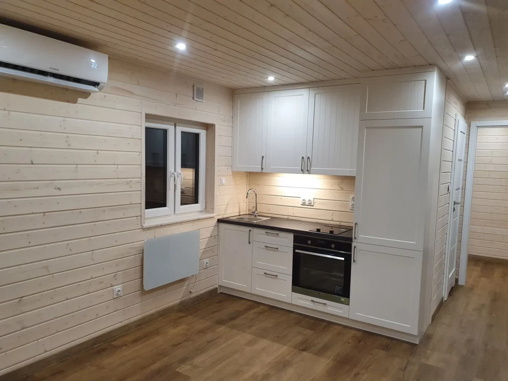 Moderne weiße Küchenzeile im Landhausstil mit integriertem Backofen, Kochfeld und LED-Beleuchtung im gemütlichen Echtholz-Innenraum eines Compact Hauses der MONO-Serie.