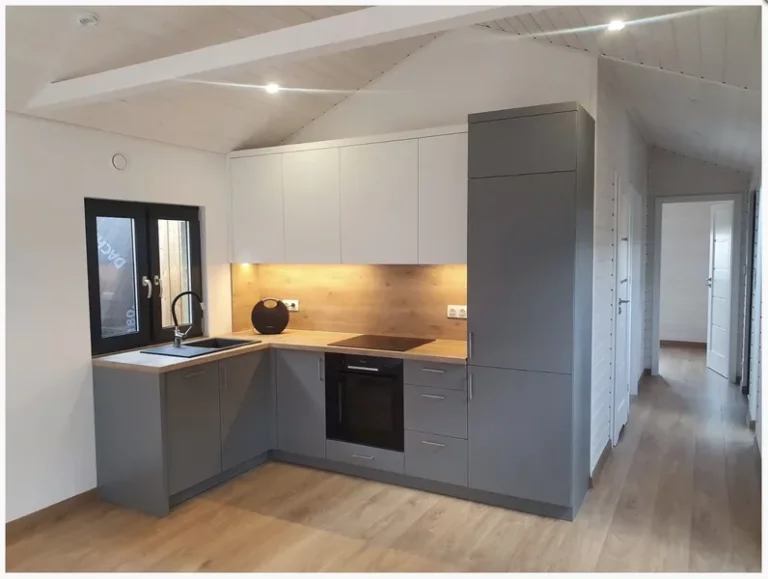Moderne L-Küche in einem Compact Haus der MONO-Serie mit anthrazitgrauen Unterschränken, weißen Oberschränken, einer Nischenrückwand in Holzoptik und LED-Unterbaubeleuchtung.