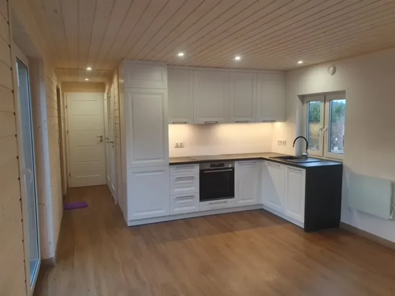 Klassische weiße Landhausküche in L-Form mit Kassettenfronten, schwarzer Arbeitsplatte und LED-Beleuchtung im offenen Wohnbereich eines Compact Hauses der MONO-Serie.