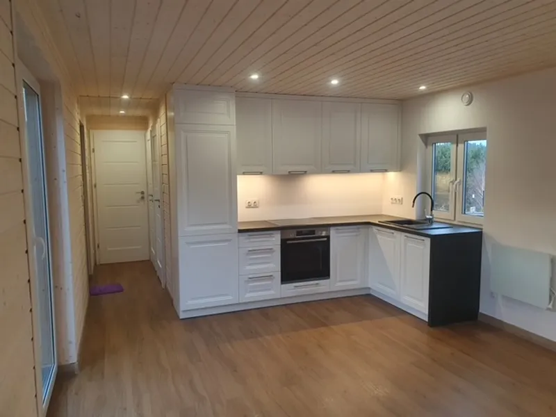 Klassische weiße Landhausküche in L-Form mit Kassettenfronten, schwarzer Arbeitsplatte und LED-Beleuchtung im offenen Wohnbereich eines Compact Hauses der MONO-Serie.