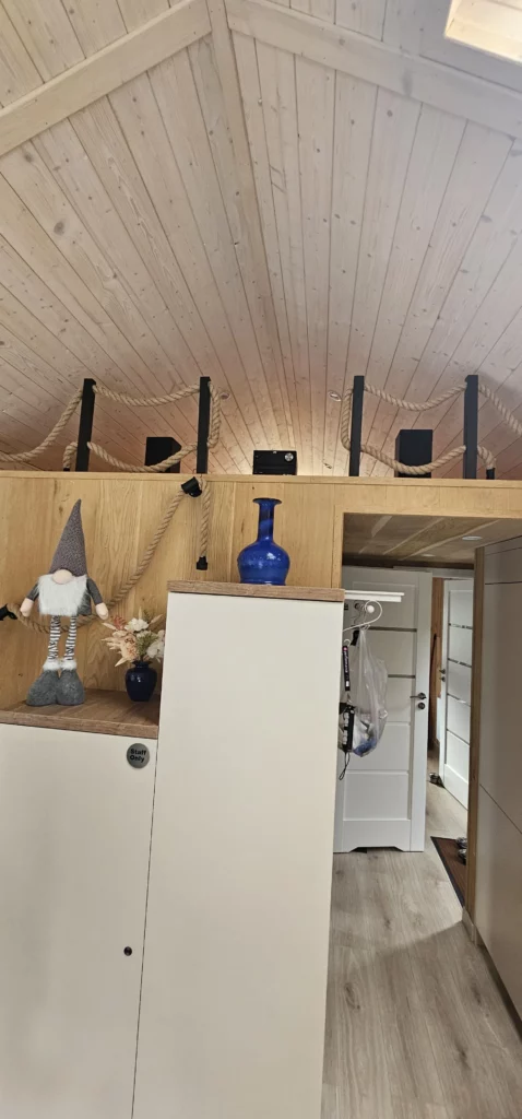 Lichtdurchfluteter Innenraum im Mobilheim der MONO-Serie von Compact Haus mit hoher Giebeldecke, einem maßgefertigten Treppenschrank, moderner Einbauküche mit Holzelementen, Einbautreppe und Dachfenster.