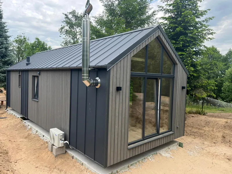 Modernes Mobilheim von Compact Haus mit Edelstahlschornstein für Kaminofen, Giebelfenstern und grauer Holzfassade.