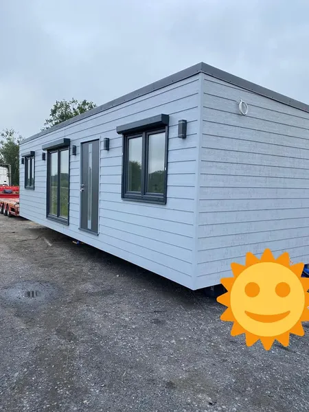 Modernes Mobilheim von Compact Haus in Hellgrau mit Flachdach, anthrazitfarbenen Rollläden und horizontaler Fassadenstruktur.
