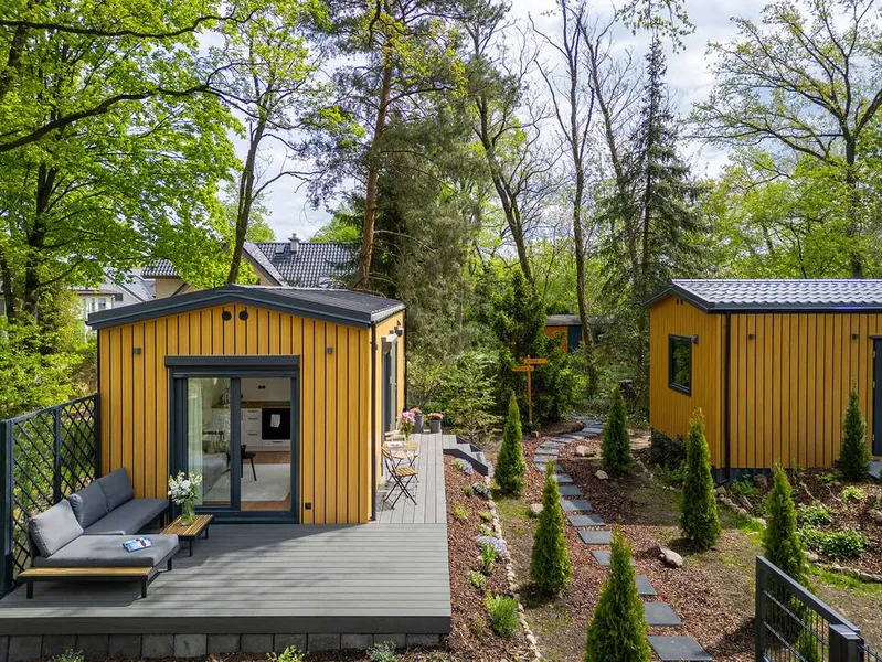 Modernes, schlüsselfertiges Mobilheim aus Holz von Compact Haus mit gemütlicher Lounge-Terrasse und Steinplattenweg in einem idyllischen Garten.