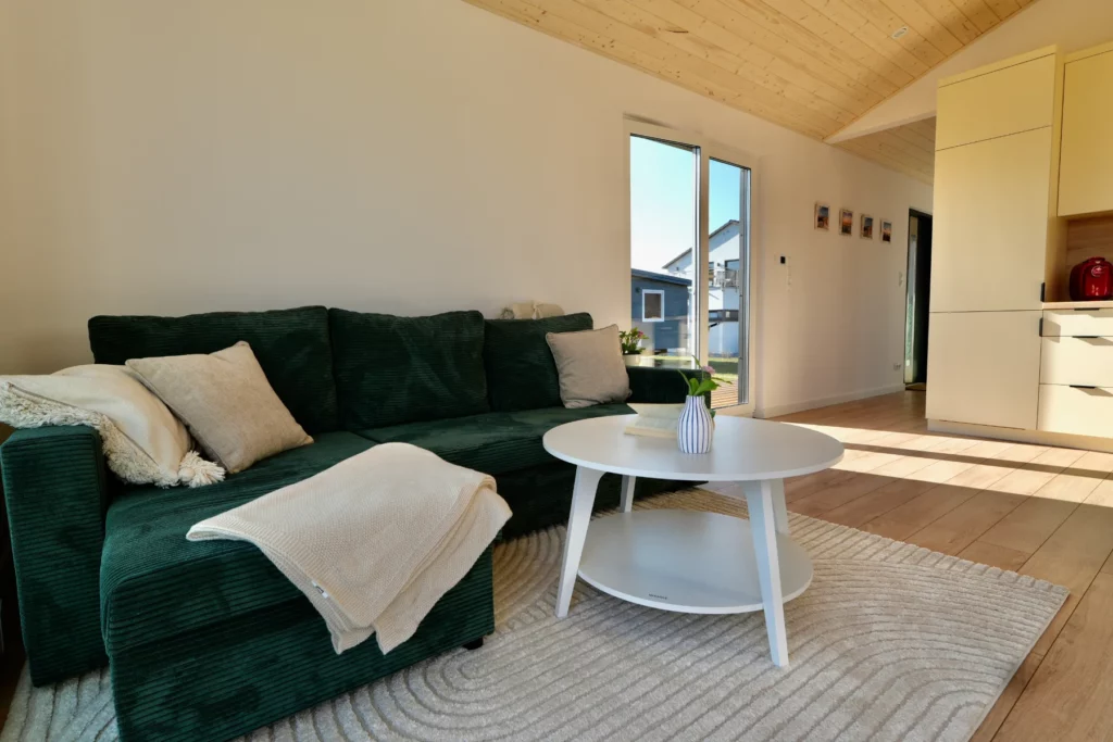 Gemuetlicher Wohnbereich mit gruenem Sofa und heller Kueche im Compact Haus Musterhaus im Unger Park Werder.
