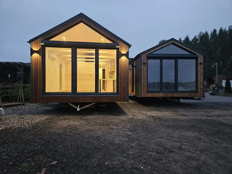 Luxuriöses Mobilheim von Compact Haus mit beleuchteter Panorama-Glasfront und Blick in die moderne Küche bei Dämmerung.