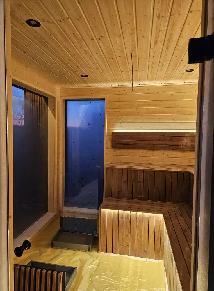 Innenansicht der eingebauten Echtholz-Sauna in einem Compact Haus der MONO-Serie mit gestuften Holzbänken, LED-Ambientebeleuchtung und Panoramafenster.