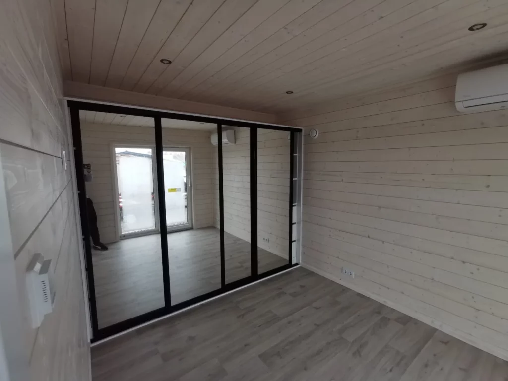 Heller Innenraum eines Compact Hauses der MONO-Serie mit skandinavischer Holzverkleidung, Klimaanlage und einem großen Einbauschrank mit verspiegelten Schiebetüren.