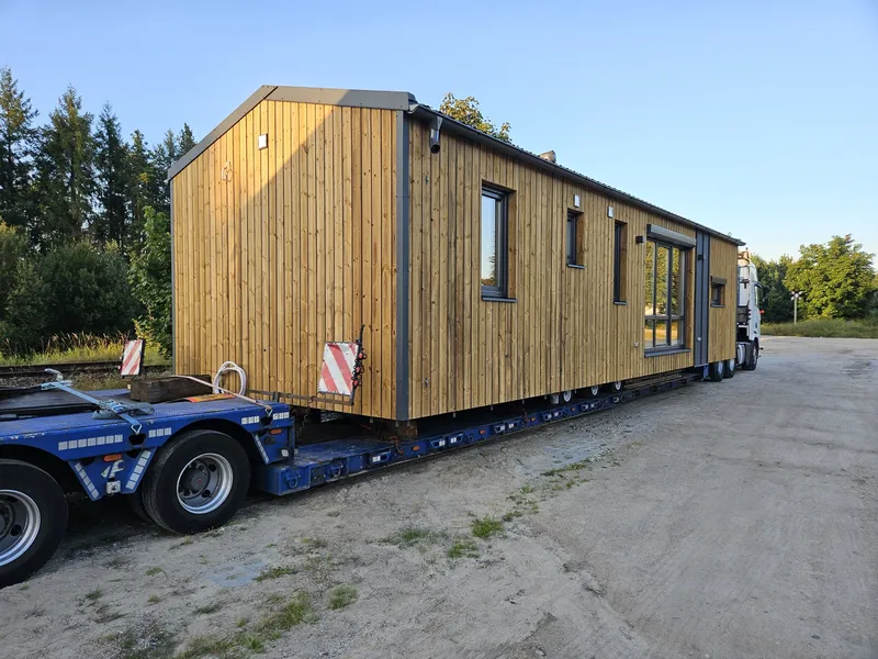 Professioneller Schwertransport und deutschlandweite Lieferung eines großen Holz-Mobilheims von Compact Haus auf einem Tieflader.