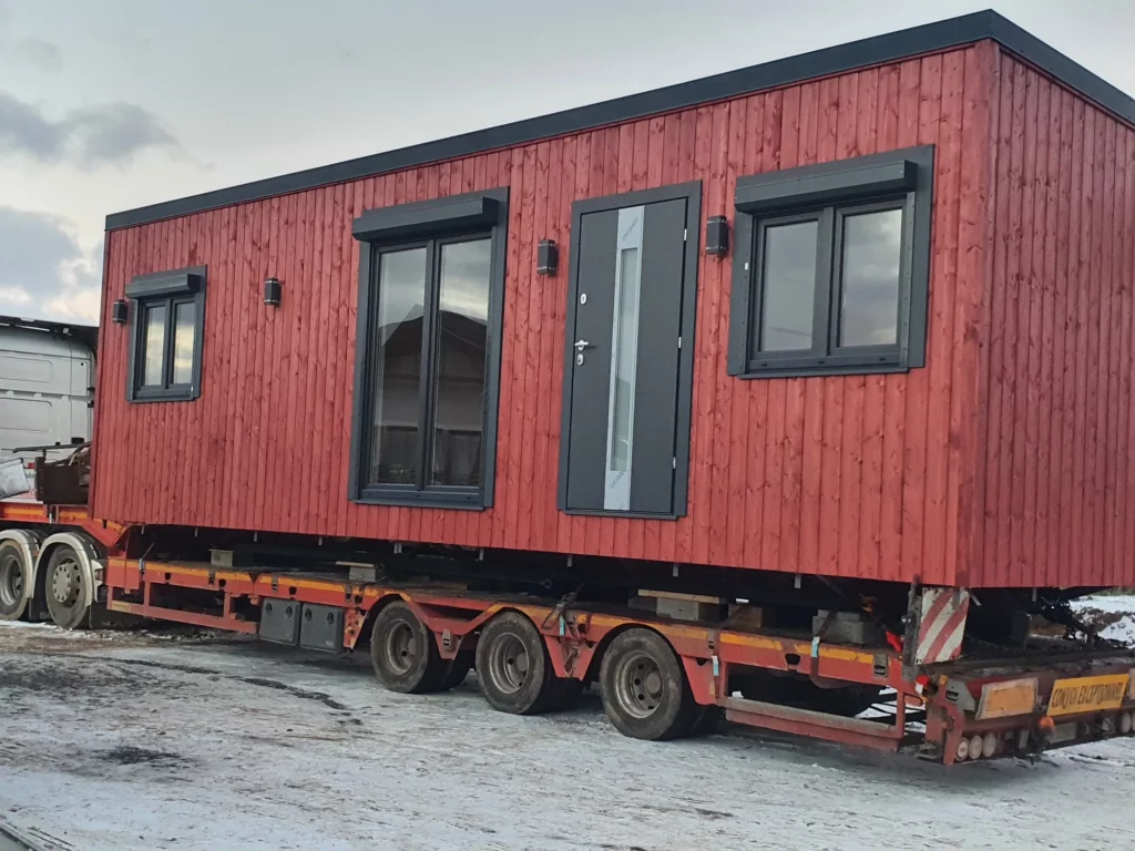 Spezialtransport eines winterfesten Mobilheims der MONO-Serie von Compact Haus in Schwedenrot auf einem Tieflader bei winterlichen Straßenverhältnissen.